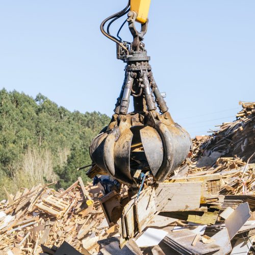 Excavator claw lifting wood debris at a recycling center, promoting sustainable waste management and environmental responsibility