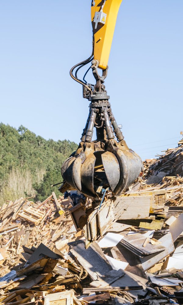 Excavator claw lifting wood debris at a recycling center, promoting sustainable waste management and environmental responsibility