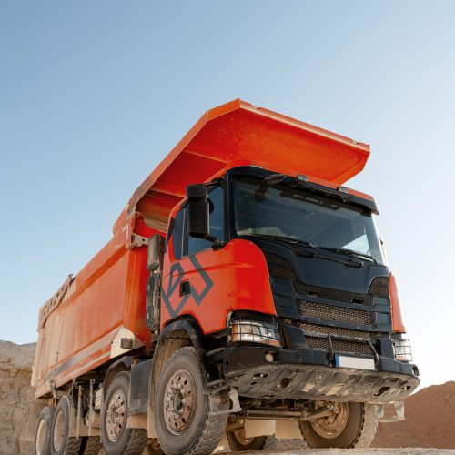 Large orange dump truck standing on quarry ground, used for hauling rocks and construction materials. Transportation concept