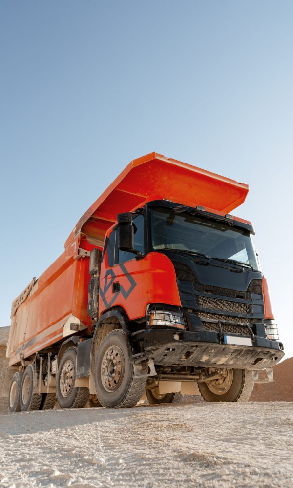Large orange dump truck standing on quarry ground, used for hauling rocks and construction materials. Transportation concept
